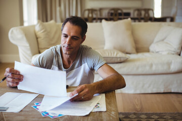 Man sorting through printed documents near sofa and wooden coffee table on living room floor