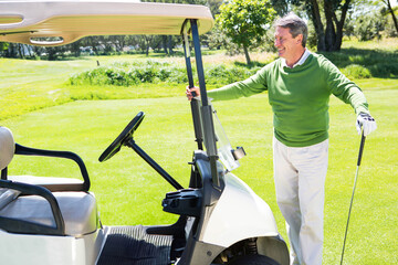 Senior African American man smiling while holding golf club beside golf cart on fairway, copy space