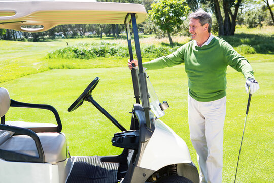 Senior African American man smiling while holding golf club beside golf cart on fairway, copy space