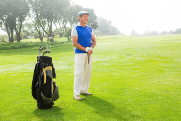 Senior man wearing sleeveless sweater and glove while holding golf club on fairway near golf bag