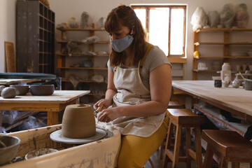 Wet clay spinning on pottery wheel and being trimmed inside ceramics workshop with wooden shelves