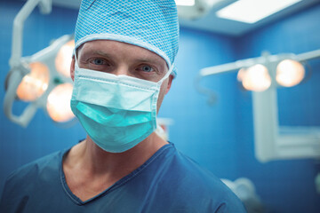 Middle-aged man standing in operating theatre wearing scrubs mask under surgical lights