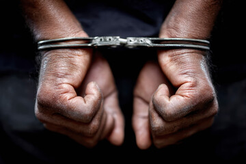 Close-up of aged, weathered hands in handcuffs against a dark background, symbolizing restraint or legal consequences.