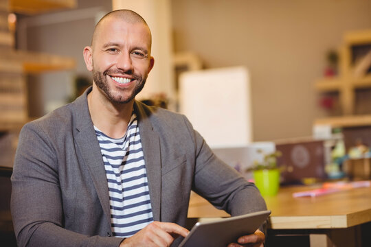 Professional sitting at desk holding digital tablet in modern office with laptop and plant