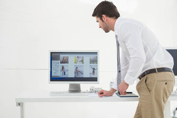 Monitor displaying thumbnails at desk in office with tablet resting beside smartphone and papers