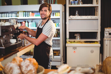 Male barista operating espresso machine behind counter in café with coffee cup and pastries