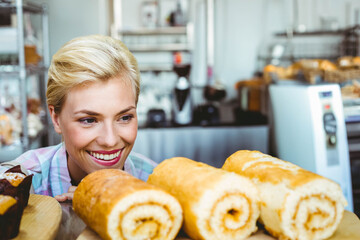 Woman leaning over pastry counter at bakery showing rolled sponge cakes on tray and mixers