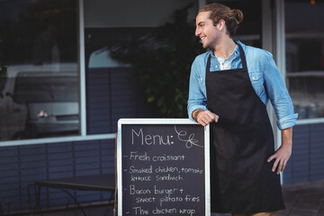Chalkboard menu displaying fresh croissants and sandwiches beside table and chairs on cafe sidewalk