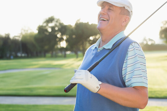 Senior man holding club and wearing visor and glove on golf course fairway, copy space
