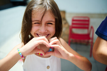 Young Girl Smiling and Making a Heart Shape with Her Hands Outdoors