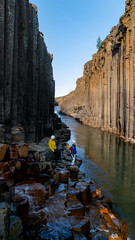 Two adventurers navigate the striking basalt columns and tranquil waters of Studlagil Canyon, a...