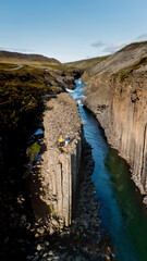Adventurers stand atop the stunning basalt columns of Studlagil Canyon in Iceland, overlooking the...