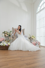 Wedding, Bride in beautiful dress sitting on sofa indoors in white studio interior, Young...