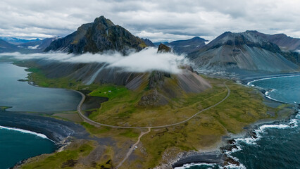 Winding roads traverse the vibrant green fields leading to towering mountains along Iceland...