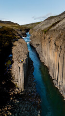 Explore the stunning beauty of Studlagil Canyon, where a vibrant river meanders between towering...