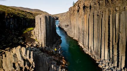 Majestic basalt columns rise steeply along the turquoise waters of Studlagil Canyon in Iceland....