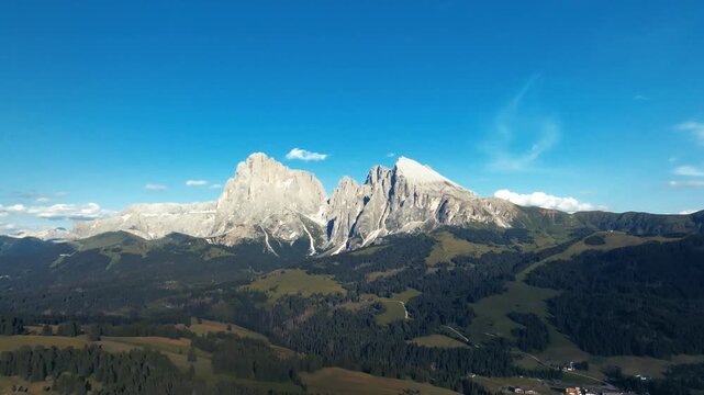 Aerial view of the rugged, grey mountains contrasting against the lush green valleys and clear blue sky near Compatsch, Trentino-Alto Adige, Italy.