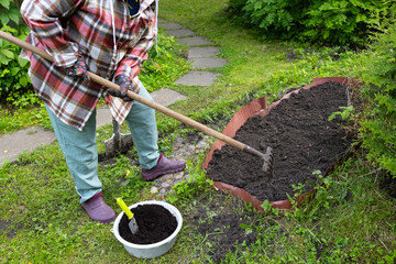 An older woman with blonde hair works in the garden. A woman is digging garden beds.