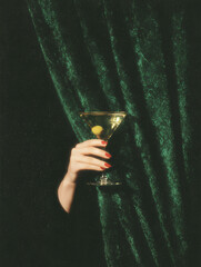 Hand with red nails holding martini glass against green velvet