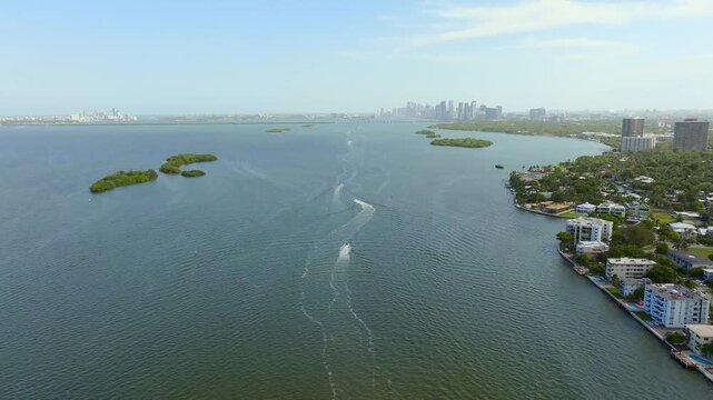 Aerial view of the 79th Street Causeway over Biscayne Bay with boats leaving white wakes, contrasting with buildings along the shoreline, North Bay Village, Florida, United States.