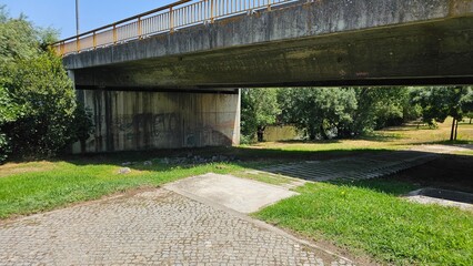 Concrete Bridge Over Green Park Path with Shadows and Graffiti
