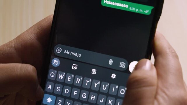 Close-up of hands holding a smartphone while enthusiastically typing a long "hello" message in Spanish.