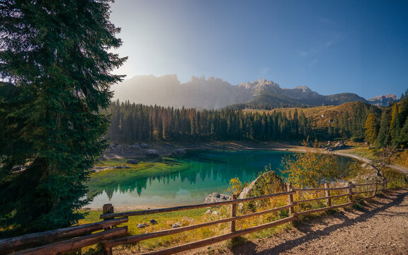 View of the emerald lake mirroring the majestic Dolomites, framed by a rustic wooden fence and verdant trees, Welschnofen, Trentino-South Tyrol, Italy.