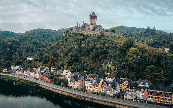 Aerial view of Reichsburg Cochem castle perched atop a verdant hill overlooking colorful buildings along the riverbank, Cochem, Rheinland-Pfalz, Germany.