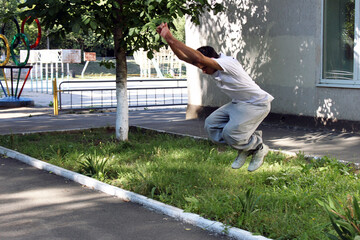 A young guy jumps over a large flowerbed with green grass	
