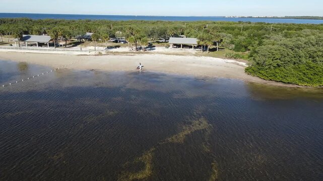 Drone flies north over water toward beach at Robert K Rees Memorial Park on sunny day in Florida, USA