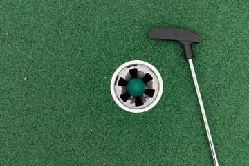 putter club and golf ball in mini golf hole