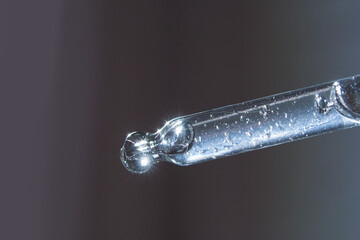 Close-up of a glass pipette with liquid droplet reflecting light on a gradient background.