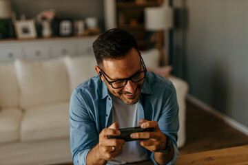 Happy man playing videogames on smartphone at home