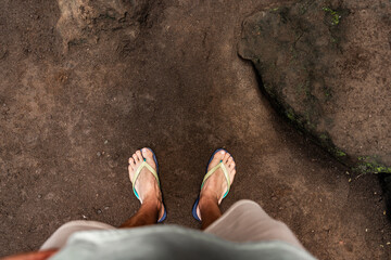 Tourist wearing flip-flops standing on dirt path near rock