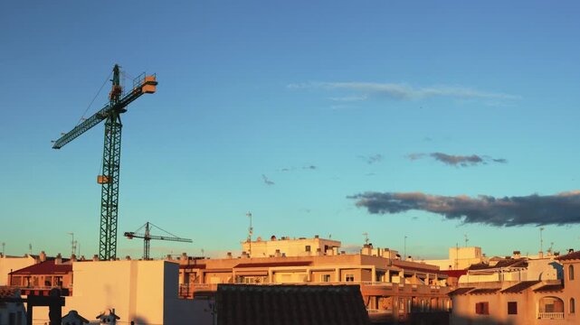 Majestic construction crane standing tall against backdrop of urban buildings as  sun gracefully descends, casting warm glow across cityscape, creating captivating urban sunset scene.timelipse
