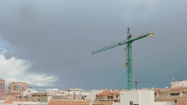 Shifting clouds revealing expansive blue sky above urban skyline, construction crane rising amid residential buildings, transforming metropolitan landscape.timelipse