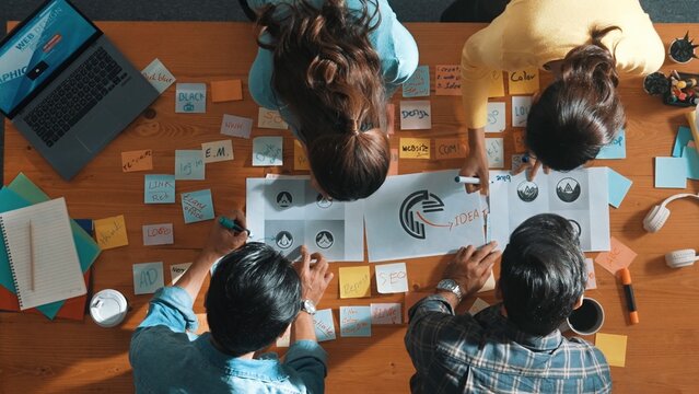 Top view of business team write graphic logo on meeting table with colorful sticky notes and design while explain idea. Project manager sharing idea and explain concept art to smart team. Symposium.