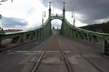 Straight tram tracks run along the bridge. A large bridge over a raging river. The steel structures...