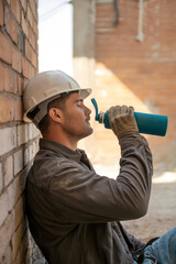 Construction Worker Taking a Hydration Break – Resting Against a Brick Wall After Labor in the Heat of the Day