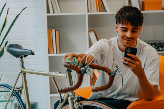 young man cleaning or preparing vintage bicycle looking at mobile phone or app