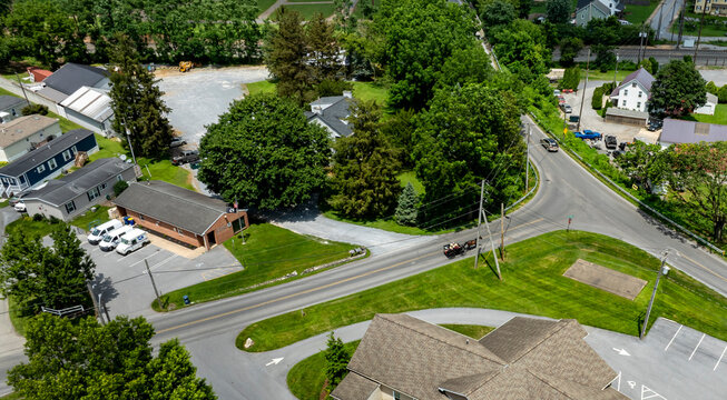 A tranquil rural intersection is captured with lush trees and buildings nearby. The scene shows a horse and carriage on quiet area with roads winding through the landscape, typical in the countryside.