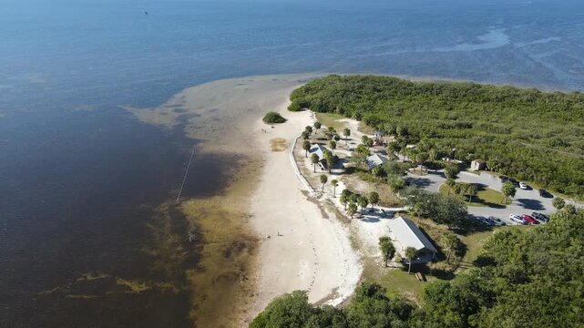 Drone orbits to the left in wide shot of Robert K Rees Memorial Park, beach, and swimming area on sunny day at Green Key in Florida, USA