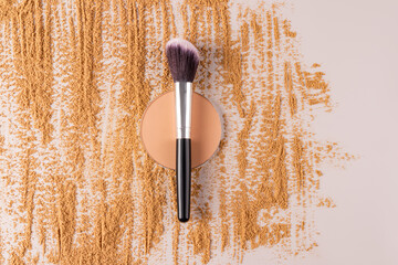A professional makeup brush rests on a block of compact powder in a natural tone and a chic sample of the texture of scattered dry powder. top view.