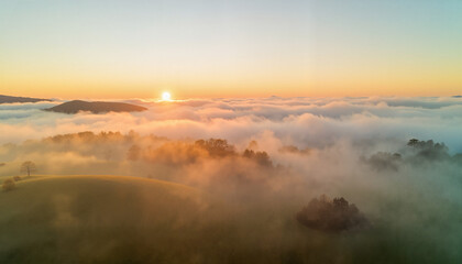 Obraz premium Aerial view of sunrise over misty hills and valleys in morning 
