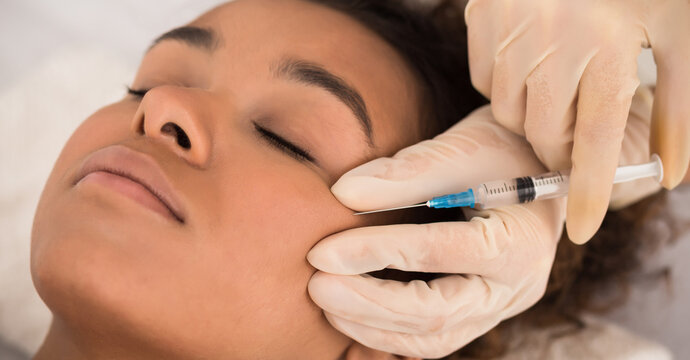 Aesthetic cosmetology. Black woman getting beauty facial injections in cheekbones