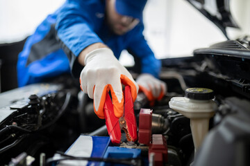Car battery jump-start process performed by a mechanic in an auto repair shop during daylight hours