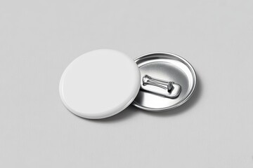 Two overlapping round pin button badges, one showing a blank white front surface, the other showing a metallic back with pin clasp, placed on a smooth light gray background