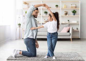 Loving arabic father dancing with his adorable little daughter at home, happy dad teaching pretty...