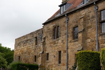 Weathered stone house with mullioned windows sits beneath cloudy sky, embraced by greenery and timeless rural calm in Mount Grace Priory - East Harlsey - North Yorkshire - UK