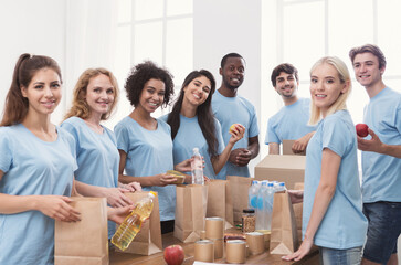 Food sorting. Group of volunteers packing donation for homeless into paper bags, working in office,...